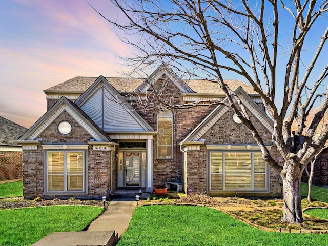 traditional home featuring brick siding, roof with shingles, and a front yard