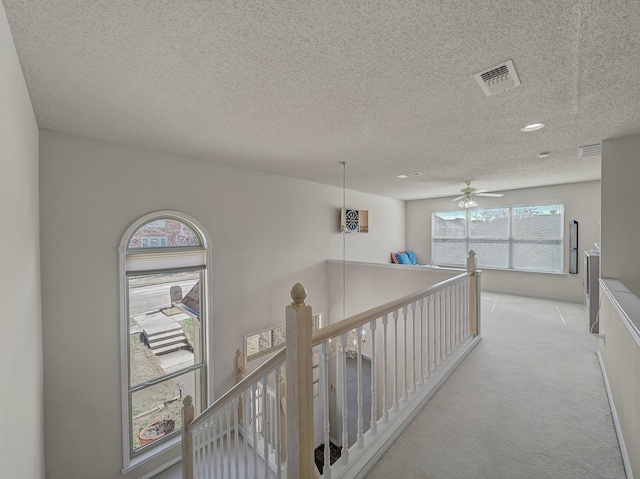 corridor featuring carpet floors, visible vents, a textured ceiling, and an upstairs landing