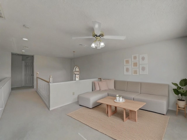 living room with a ceiling fan, visible vents, light colored carpet, and a textured ceiling