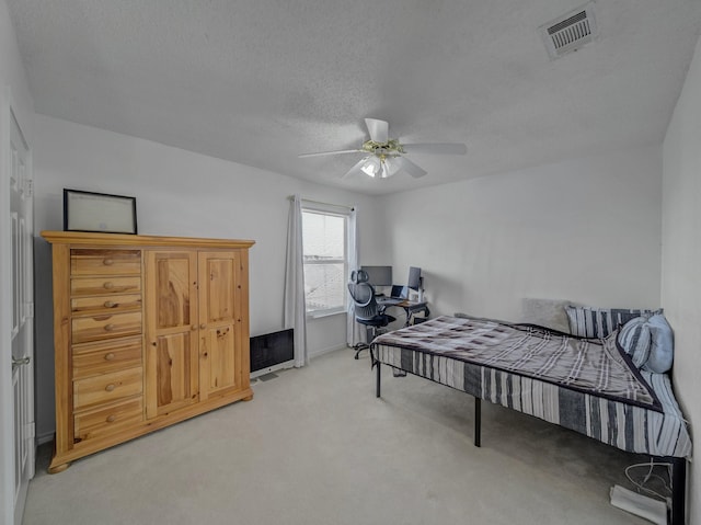 bedroom with light carpet, a ceiling fan, visible vents, and a textured ceiling