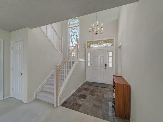 carpeted foyer entrance with stairs, a textured ceiling, an inviting chandelier, and baseboards