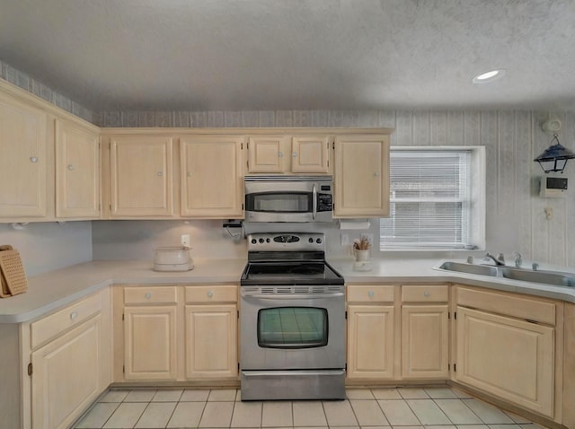 kitchen featuring a textured ceiling, a sink, light countertops, appliances with stainless steel finishes, and light brown cabinetry