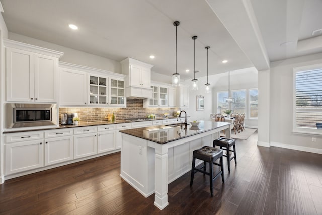 kitchen with dark wood finished floors, dark countertops, backsplash, appliances with stainless steel finishes, and an island with sink