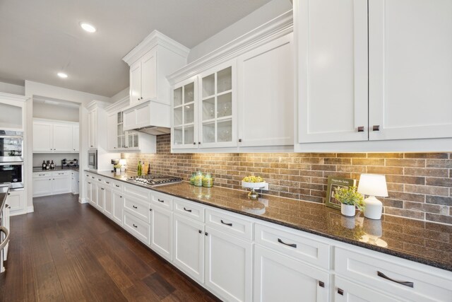 kitchen featuring premium range hood, appliances with stainless steel finishes, dark hardwood / wood-style floors, dark stone counters, and white cabinets