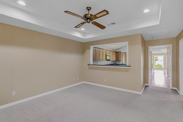 unfurnished living room with ceiling fan, a tray ceiling, and light carpet