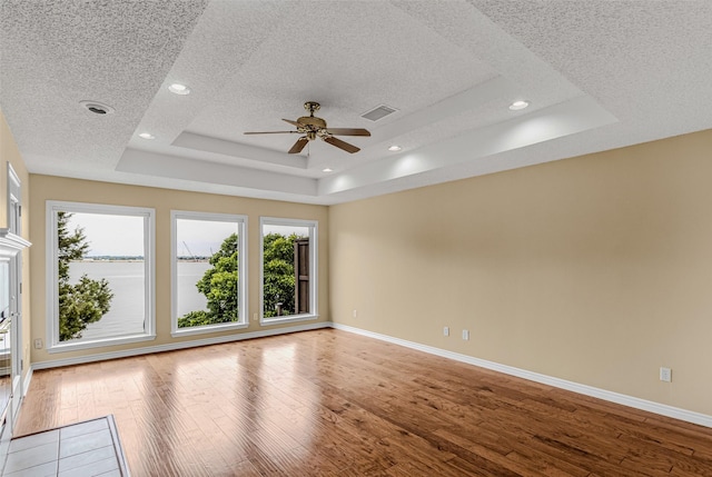 empty room featuring ceiling fan, a textured ceiling, light wood-type flooring, and a tray ceiling