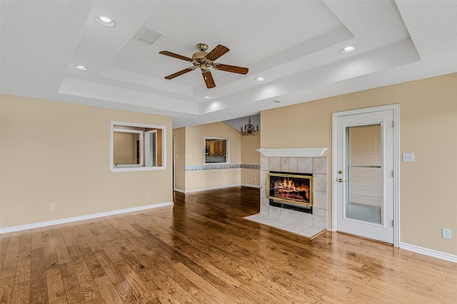 unfurnished living room with light hardwood / wood-style flooring, ceiling fan, a textured ceiling, a tiled fireplace, and a raised ceiling