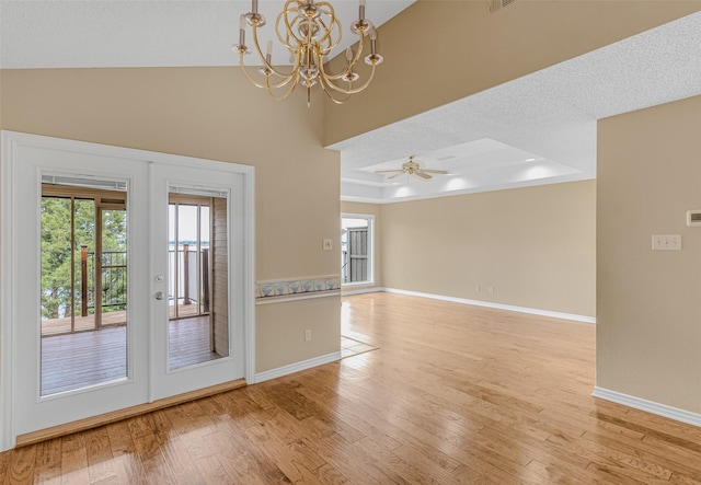 spare room featuring french doors, ceiling fan with notable chandelier, light wood-type flooring, and a tray ceiling