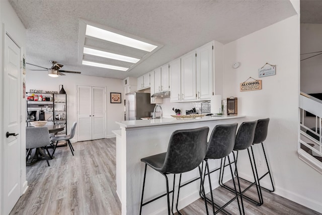 kitchen with a breakfast bar, white cabinetry, a textured ceiling, stainless steel fridge, and kitchen peninsula