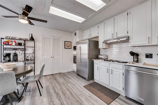 kitchen featuring light hardwood / wood-style flooring, a textured ceiling, stainless steel appliances, decorative backsplash, and white cabinets