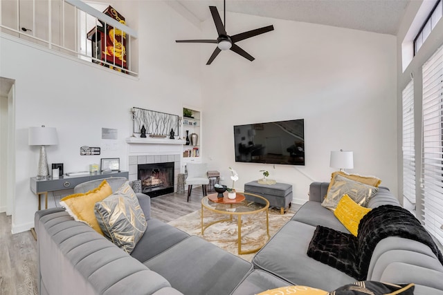 living room with ceiling fan, high vaulted ceiling, light hardwood / wood-style floors, and a tile fireplace