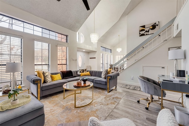 living room with ceiling fan with notable chandelier, a textured ceiling, high vaulted ceiling, and light hardwood / wood-style flooring