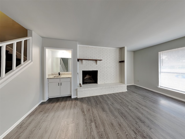 unfurnished living room featuring sink, light hardwood / wood-style floors, and a brick fireplace