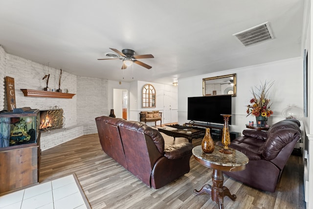 living room featuring hardwood / wood-style floors, a fireplace, ceiling fan, and brick wall