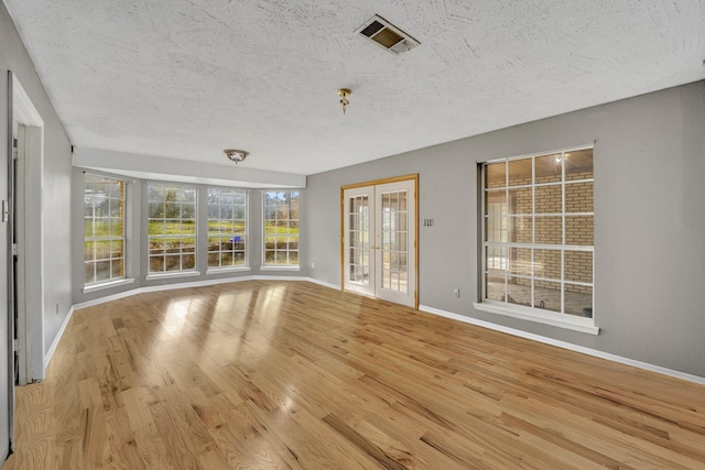 interior space with light hardwood / wood-style flooring, french doors, and a textured ceiling