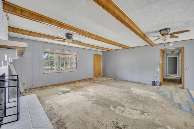 unfurnished living room featuring beamed ceiling, ceiling fan, and wood walls