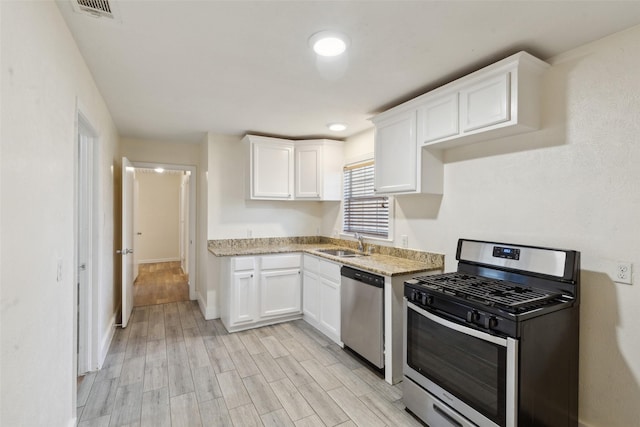 kitchen with sink, light stone counters, light hardwood / wood-style flooring, appliances with stainless steel finishes, and white cabinets