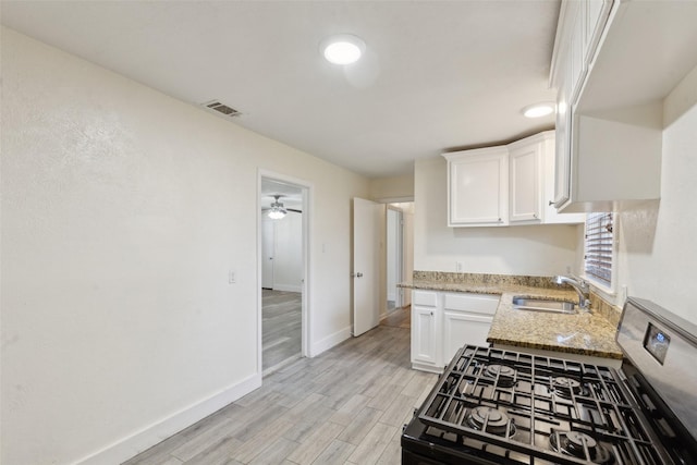 kitchen featuring sink, white cabinets, light stone counters, light hardwood / wood-style floors, and gas stove