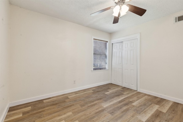 unfurnished bedroom featuring light hardwood / wood-style floors, a textured ceiling, ceiling fan, and a closet