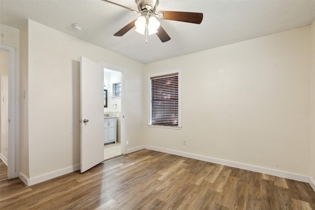 unfurnished bedroom featuring ceiling fan, wood-type flooring, ensuite bath, and a textured ceiling