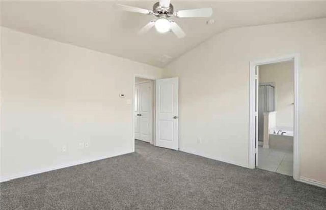 unfurnished bedroom featuring ceiling fan, ensuite bathroom, vaulted ceiling, and dark colored carpet