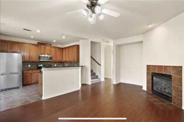 kitchen featuring stainless steel appliances, tasteful backsplash, dark wood-type flooring, and a tiled fireplace