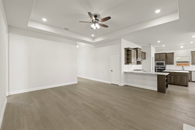 unfurnished living room featuring sink, a tray ceiling, ceiling fan, and hardwood / wood-style flooring