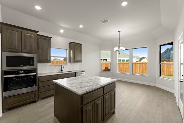 kitchen with vaulted ceiling, a kitchen island, appliances with stainless steel finishes, sink, and decorative backsplash