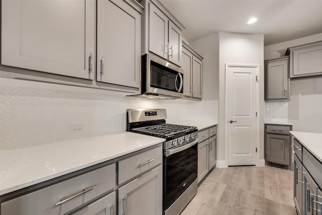 kitchen with gray cabinets, appliances with stainless steel finishes, light wood-type flooring, and decorative backsplash