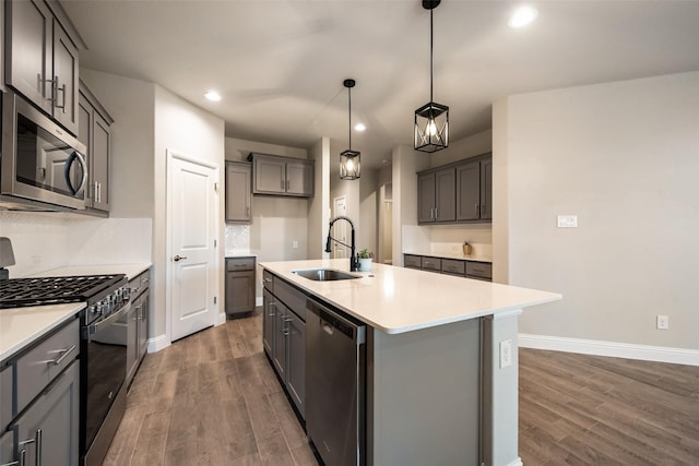 kitchen featuring dark wood-type flooring, sink, hanging light fixtures, a center island with sink, and appliances with stainless steel finishes