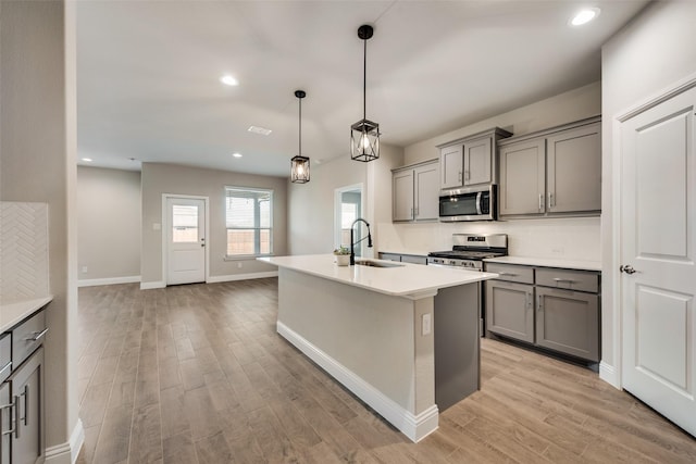 kitchen with gray cabinets, appliances with stainless steel finishes, pendant lighting, sink, and a kitchen island with sink