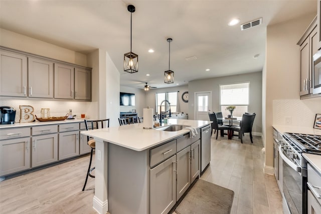 kitchen featuring appliances with stainless steel finishes, sink, a breakfast bar area, hanging light fixtures, and a center island with sink