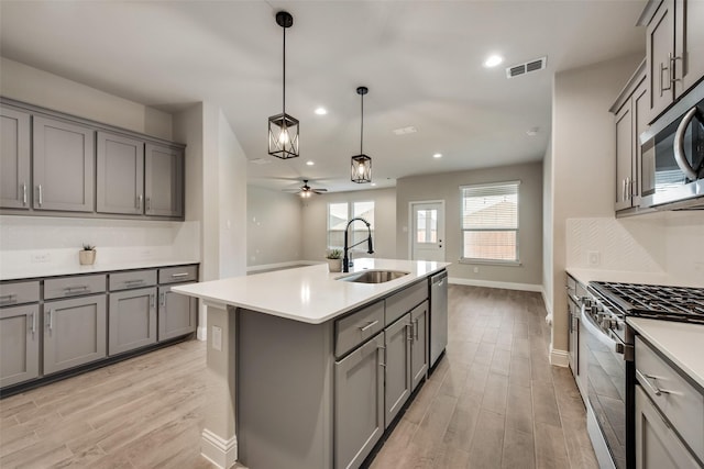 kitchen with sink, gray cabinets, an island with sink, and appliances with stainless steel finishes