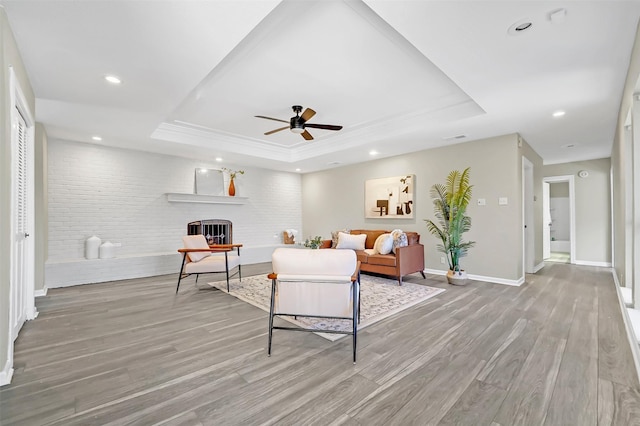 living room with a raised ceiling, ceiling fan, a brick fireplace, and light hardwood / wood-style floors