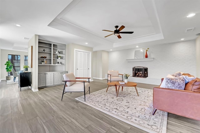 living room featuring a raised ceiling, ceiling fan, a large fireplace, and light hardwood / wood-style floors