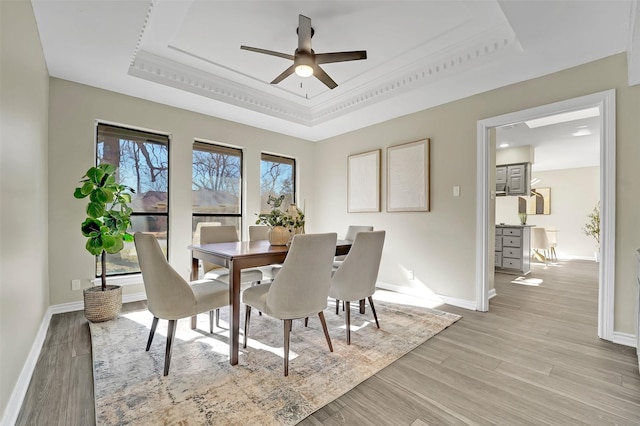 dining area with a raised ceiling, ornamental molding, ceiling fan, and light hardwood / wood-style flooring