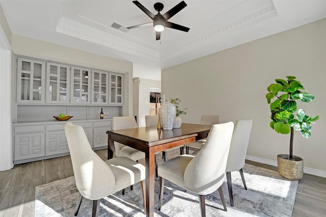 dining space featuring ornamental molding, light hardwood / wood-style floors, a raised ceiling, and ceiling fan