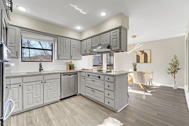 kitchen with sink, light stone countertops, decorative light fixtures, stainless steel dishwasher, and kitchen peninsula