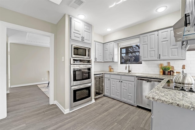 kitchen featuring appliances with stainless steel finishes, sink, wine cooler, light stone counters, and light hardwood / wood-style flooring