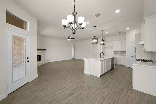 kitchen with a stone fireplace, sink, white cabinetry, decorative light fixtures, and a center island with sink