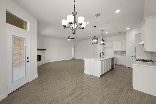 kitchen with a stone fireplace, sink, white cabinetry, hanging light fixtures, and a center island with sink