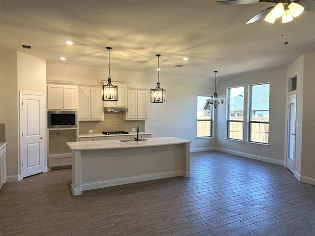 kitchen with stainless steel microwave, sink, white cabinetry, and a kitchen island with sink