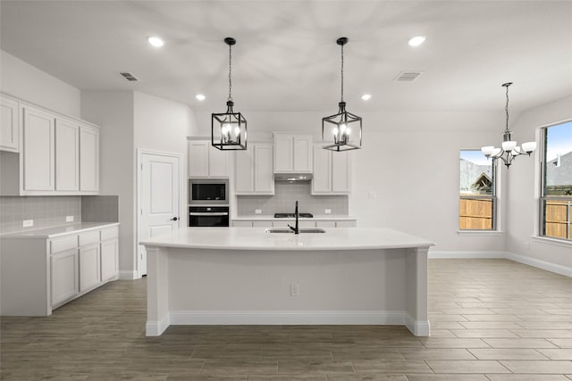 kitchen featuring built in microwave, white cabinetry, hanging light fixtures, black oven, and a kitchen island with sink