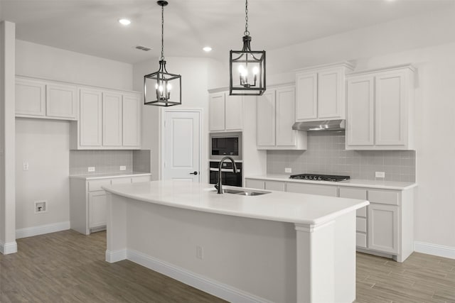 kitchen featuring built in microwave, sink, a kitchen island with sink, and white cabinets