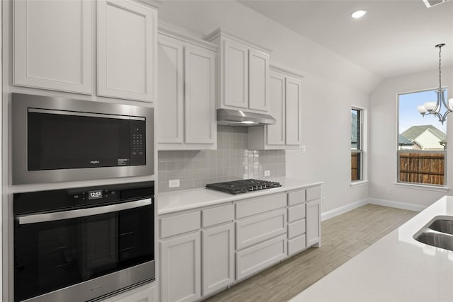 kitchen with hanging light fixtures, stainless steel appliances, white cabinets, decorative backsplash, and a chandelier