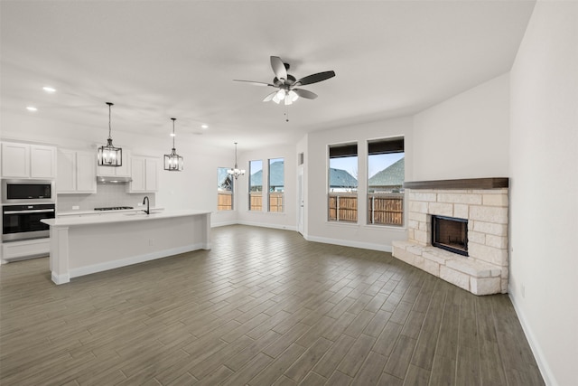 kitchen with built in microwave, white cabinetry, an island with sink, pendant lighting, and oven