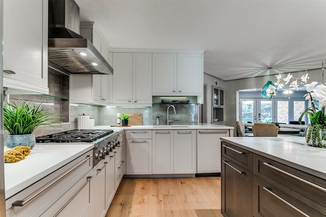 kitchen featuring white cabinetry, hanging light fixtures, stainless steel gas stovetop, decorative backsplash, and wall chimney range hood