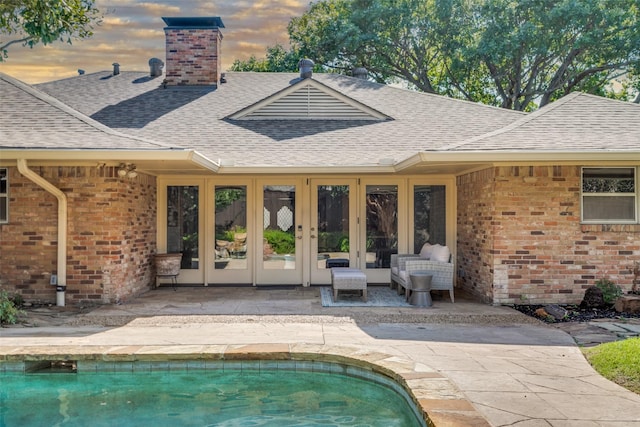 pool at dusk featuring french doors and a patio area