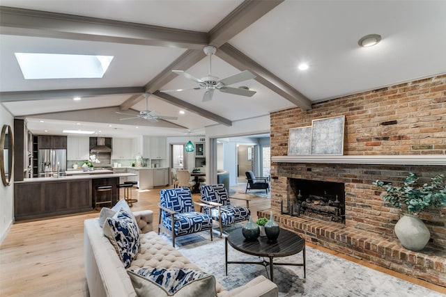 living room with a fireplace, light hardwood / wood-style flooring, vaulted ceiling with skylight, and brick wall