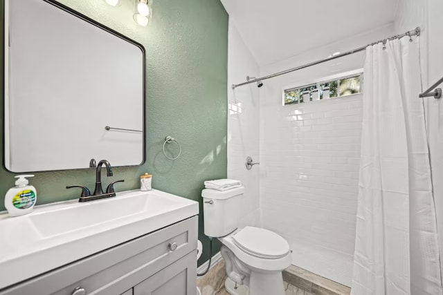 full bath featuring toilet, vanity, tiled shower, and a textured wall